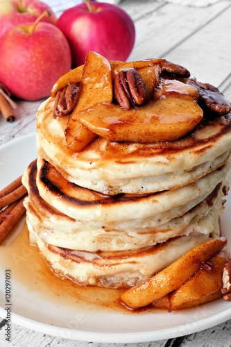 Autumn pancake stack with baked apples, pecans and cinnamon topped with maple syrup, close up