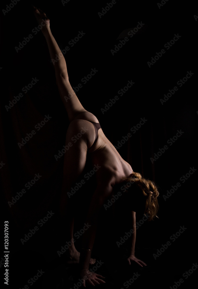 Back view of beautiful female bottom, naked body on a black background. slim woman doing yoga asanas