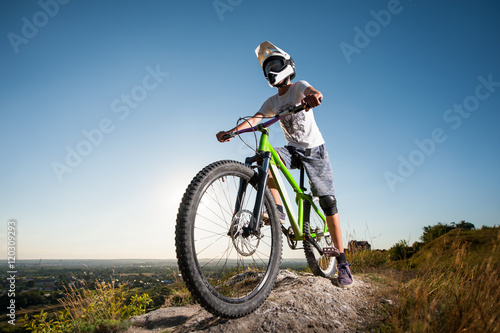 Cyclist in helmet and glasses stay on the mountain bicycle at the hill under blue sky against blue sky and looking into the distance. Wide angle view