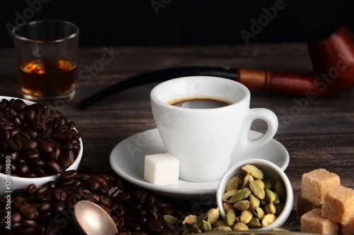Cup of espresso coffee, sugar, cane sugar, coffee beans, brandy, cardamom, Special light, selective focus. 