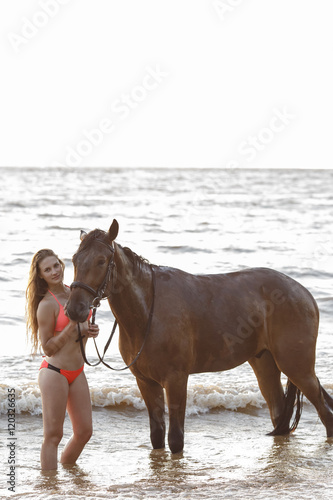 Young beautiful woman ride walk and pose with her horse on the river sunset background sun beams strong back light