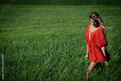 Portrait of beautiful girl dressed in a red tunic and denim shorts walking in field