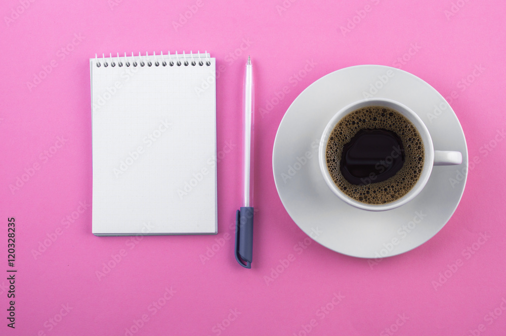 White cup of coffee, notepad, pen on a pink background White cup of coffee, notepad, pen on a pink background