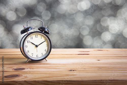 Vintage clock on wooden table over bokeh background