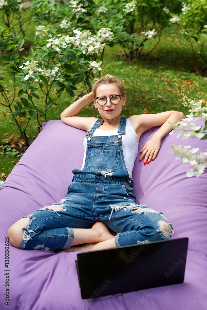 Obraz premium Freelancer working in the garden. Writing, surfing in the internet. Young woman relaxing and having fun in park area. Distance education, freelance concept.