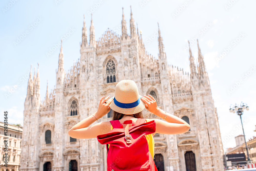 Obraz premium Back view on young tourist with backpack and hat looking on the famous Duomo cathedral in Milan. Having great vacations in Milan
