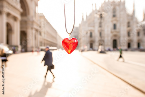 Red pendant in form of the heart on the central square background with Duomo cathedral in Milan. © rh2010
