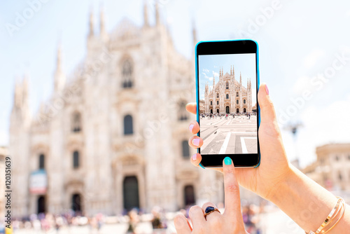 Female hands holding smart phone with photo of Duomo cathedral in the center of Milan city