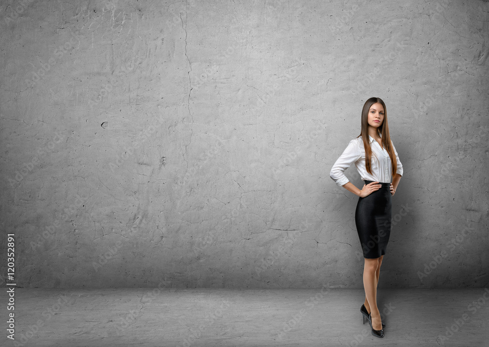 Young businesswoman holding hands on her waist in the background of concrete wall Young businesswoman holding hands on her waist in the background of concrete wall