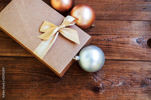 Gift box with gold bow with hristmas balls on wood background