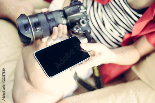 Person working with DSLR camera and smartphone, light background. Close up top view mockup screen
