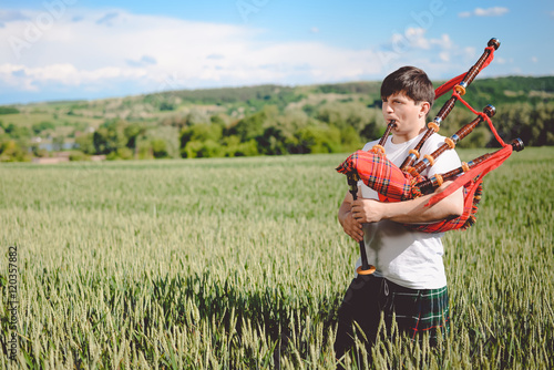 Male enjoying playing pipes in traditional kilt on green outdoors copy space summer field.