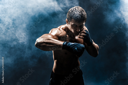 Muscular kickbox or muay thai fighter punching in smoke. © zamuruev