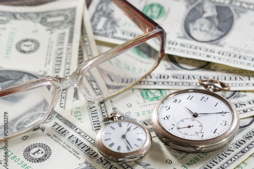 Time is money finance concept with old vintage clocks, dollar bills, spectacles