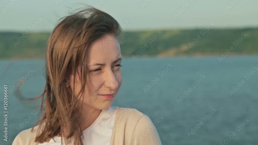 Young beautiful woman standing on deck of cruise ship, smiling and looking forward. Sunrise light, golden hour. Strong wind waving her hair. Close up shot of woman's face Young beautiful woman standing on deck of cruise ship, smiling and looking forward. Sunrise light, golden hour. Strong wind waving her hair. Close up shot of woman's face