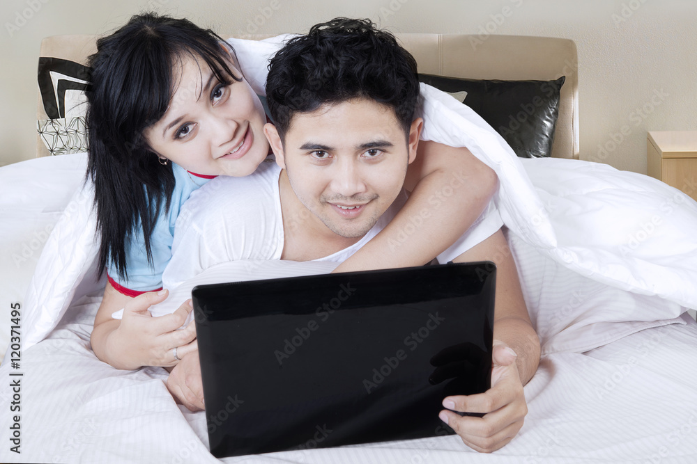 Young couple with laptop in bedroom Young couple with laptop in bedroom
