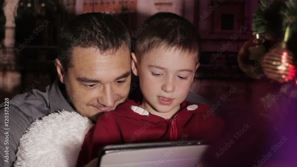 lovely family sharing digital tablet near the wood stove on a winter evening, enjoying the warm Christmas atmosphere in their living room, mother and child wearing a hat of Santa Claus lovely family sharing digital tablet near the wood stove on a winter evening, enjoying the warm Christmas atmosphere in their living room, mother and child wearing a hat of Santa Claus