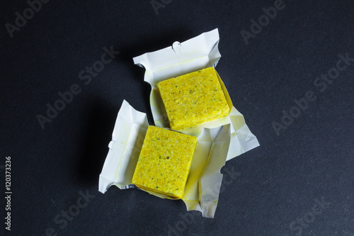 Dehydrated bouillon stock cube salty meat and vegetables aromatic yellow spice, ingredient single whole condiment portion wrapped, open in paper pack
