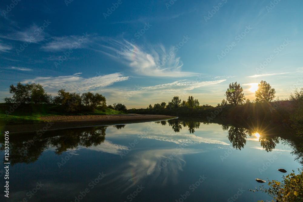 Mirror reflection of blue sky, clouds and sunset colors in wild river, in spring