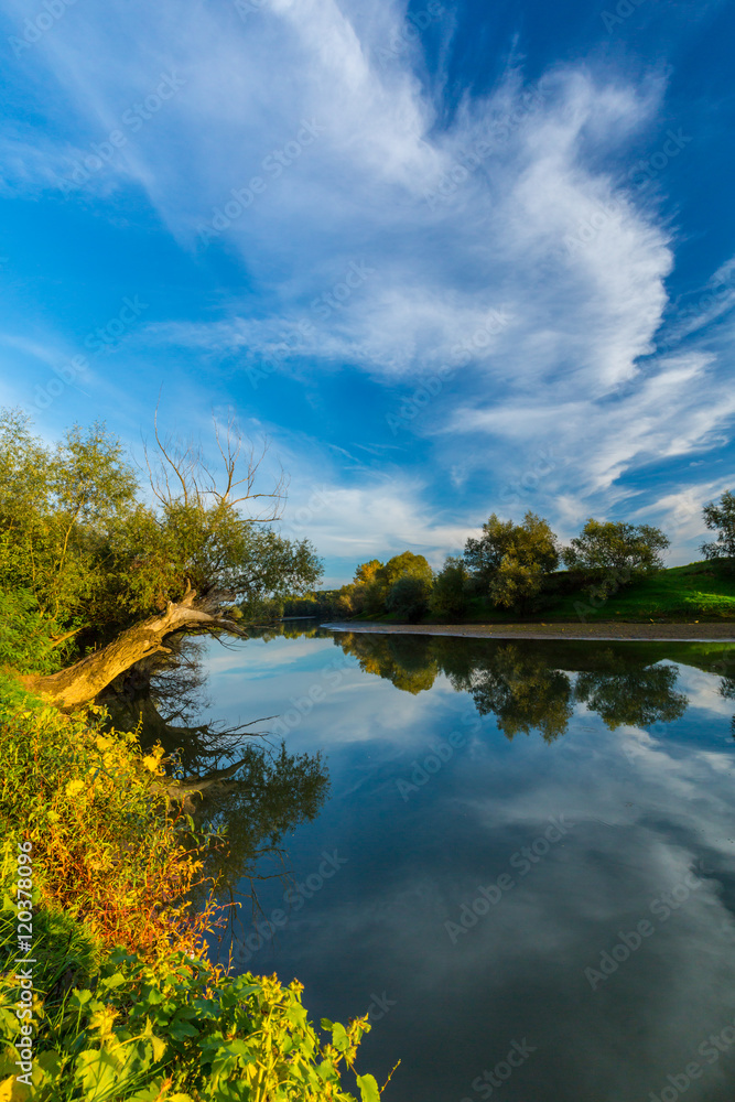 Mirror reflection of blue sky, clouds and sunset colors in wild river, in spring