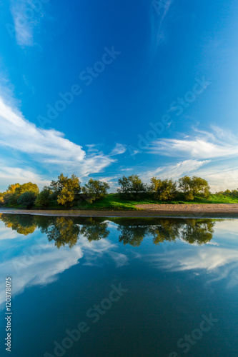 Mirror reflection of blue sky  clouds and sunset colors in wild river  in spring