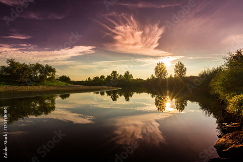 Mirror reflection of blue sky, clouds and sunset colors in wild river, in spring