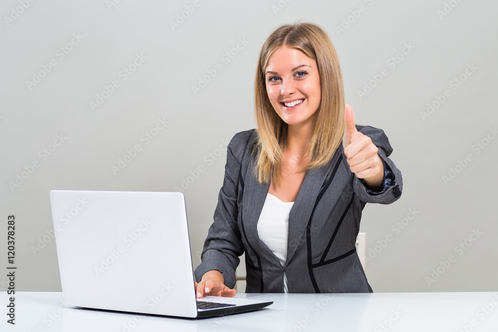 Beautiful businesswoman is sitting at the table,using laptop and showing thumb up.
Beautiful businesswoman is sitting at the table,using laptop and showing thumb up.