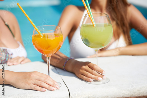 young women relaxing at swimming pool drinking a cocktail