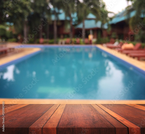 Empty brown wooden table surface and swimming pool blur background with bokeh image  for product display montage can be used for montage or display your products