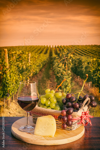 Fototapeta Naklejka Na Ścianę i Meble -  Glass of red wine in front of a vineyard at sunset