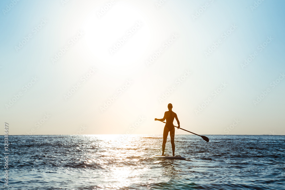 Silhouette of young beautiful girl surfing in sea at sunrise.