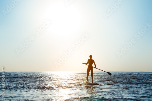 Silhouette of young beautiful girl surfing in sea at sunrise.