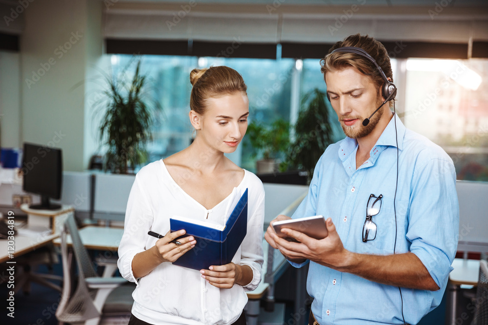 Colleagues smiling, speaking, holding tablet and notebook, over office background. Colleagues smiling, speaking, holding tablet and notebook, over office background.