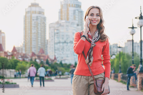 Walking by city. Attractive young woman talking on mobile phone outdoors.