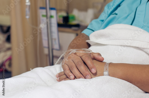 Hand of Male patient lying on a hospital bed receiving saline.