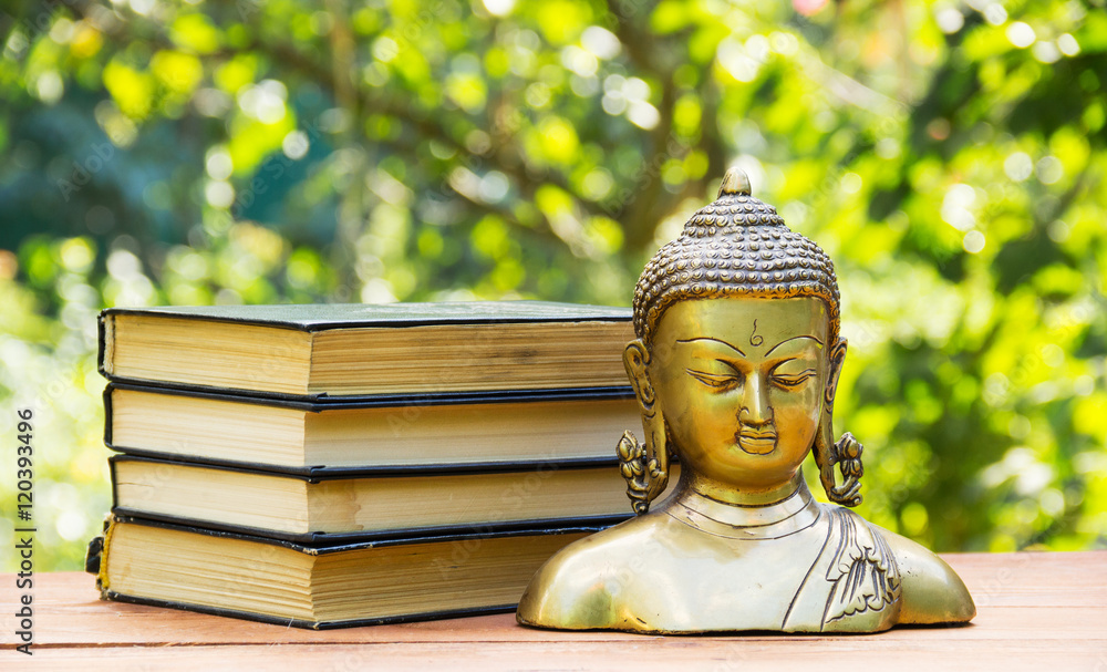 Buddha statue and stack of old books. Spa concept. Education concept. Calmness and tranquility. Copy space. Natural blur green background.
