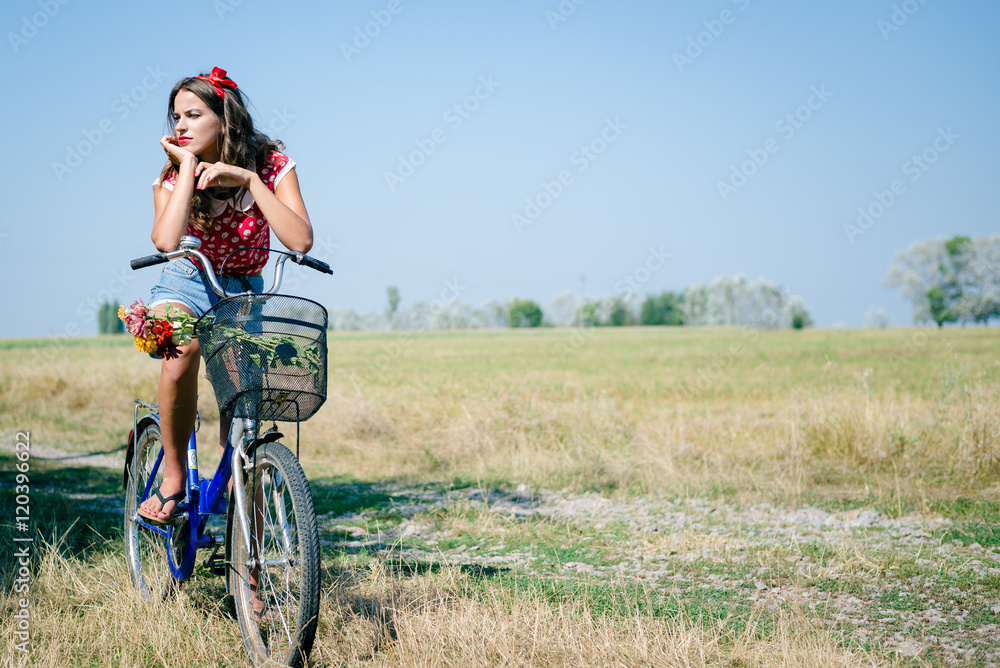 Young pinup woman cycling in fields under bright blue summer sky copy space image Young pinup woman cycling in fields under bright blue summer sky copy space image