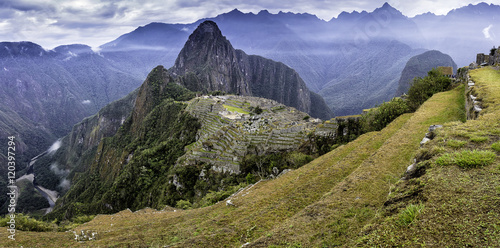 Panoramic shot of the lost Inca city of Machu Picchu with yellow grassland, clouds and Huayna Picchu in the background. photo
