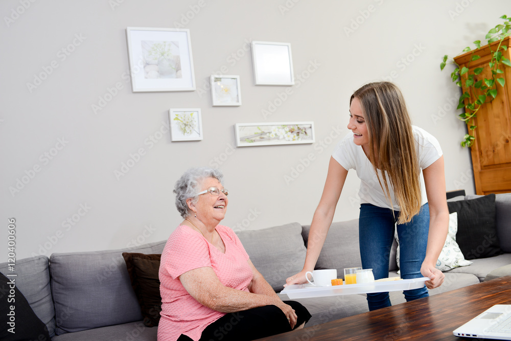 cheerful young girl serving breakfast to an elderly woman at home cheerful young girl serving breakfast to an elderly woman at home