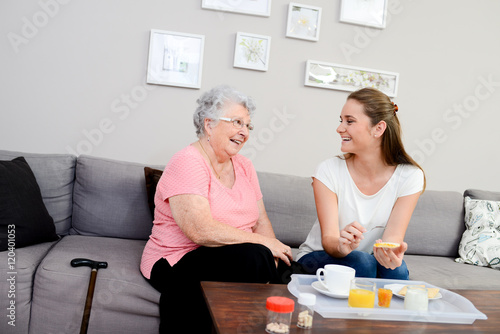 cheerful young girl serving breakfast to an elderly woman at home photo