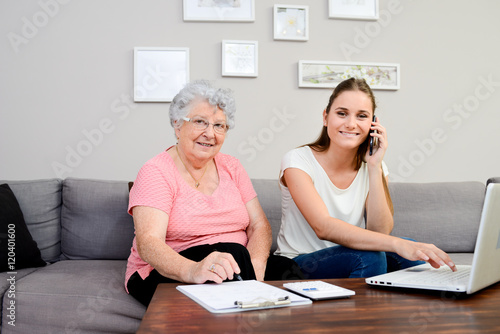 фотографія cheerful young woman helping an old person doing paperwork and telephone call