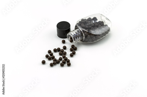 Фотография Black pills of traditional medicine or Black bolus near bottle on white backgrou