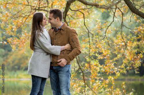 Romantic couple relaxing in autumn park, cuddling, kissing, laughing, enjoying fresh air, beautiful nature, nice fall weather. Beloved spending time together. Yellow leaves in background