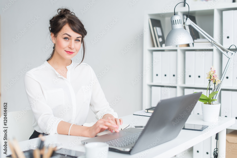 Close-up portrait of a businesswoman at her workplace working with pc, looking in camera, wearing office suit. Close-up portrait of a businesswoman at her workplace working with pc, looking in camera, wearing office suit.