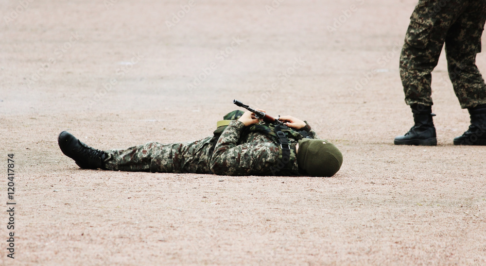 Fototapeta premium Man in Military camouflage clothing and a mask lying on his back the sand with machine guns in hand during the demonstration performance of special response team