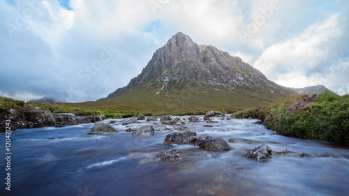Beautiful river with rocks in it flowing in a scottish Valley next to a huge mountain in the background.  © Puravidaniel