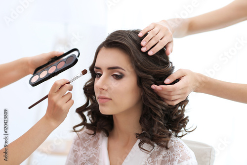 Makeup artist and hairdresser preparing bride before her wedding