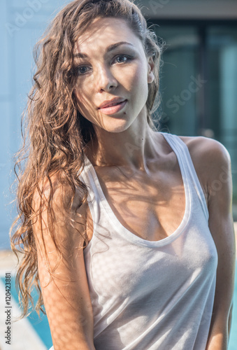 Closeup portrait of beautiful brunette woman wearing white see tgrough top looking into the camera by the outdoor pool during summer day photo