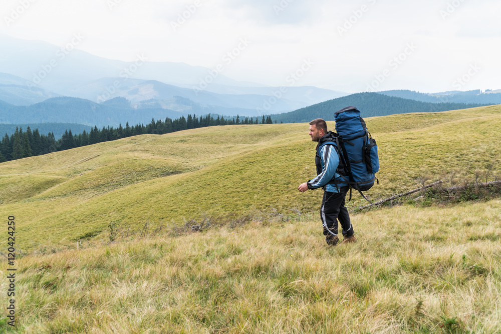 Man tourist with a big backpack goes on the grass against mountains