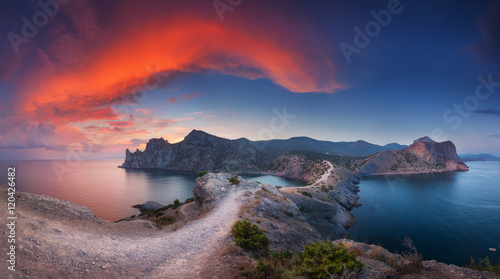 Beautiful panoramic landscape with mountains, sea, blue sky and beautiful colorful red clouds at sunset in Crimea. Sunset in mountains. Path in rock. Nature background. Vibrant landscape in twilight. 